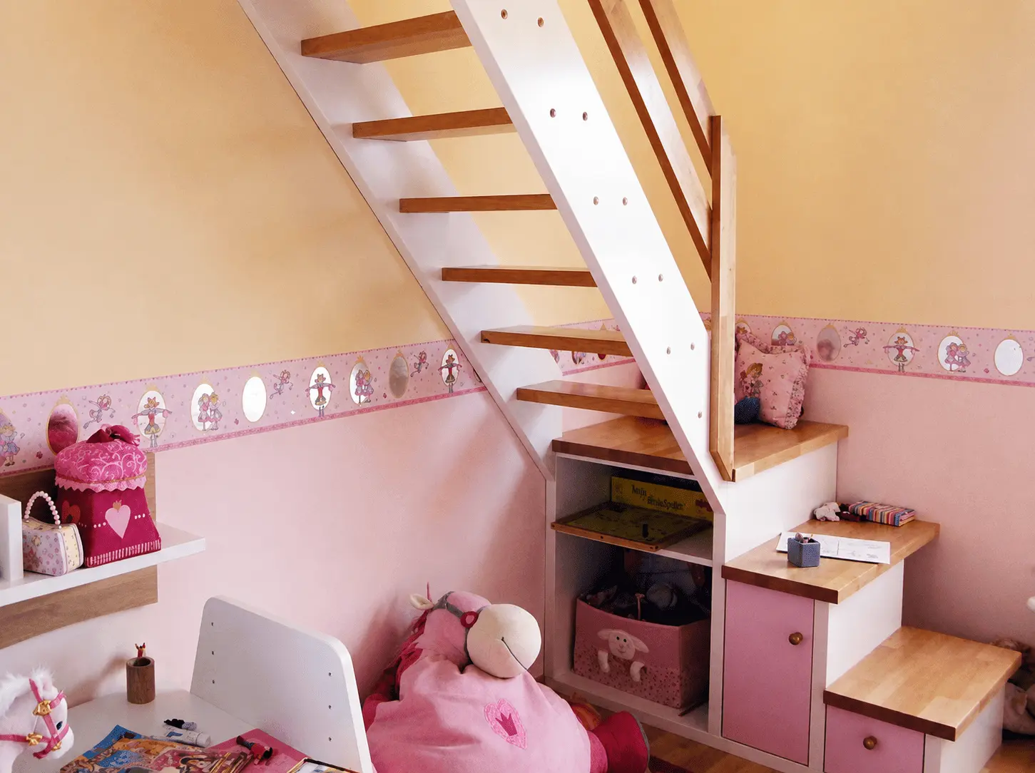 Kinderzimmer mit rosa Tapete und dekorativer Bordüre unter einer Holztreppe