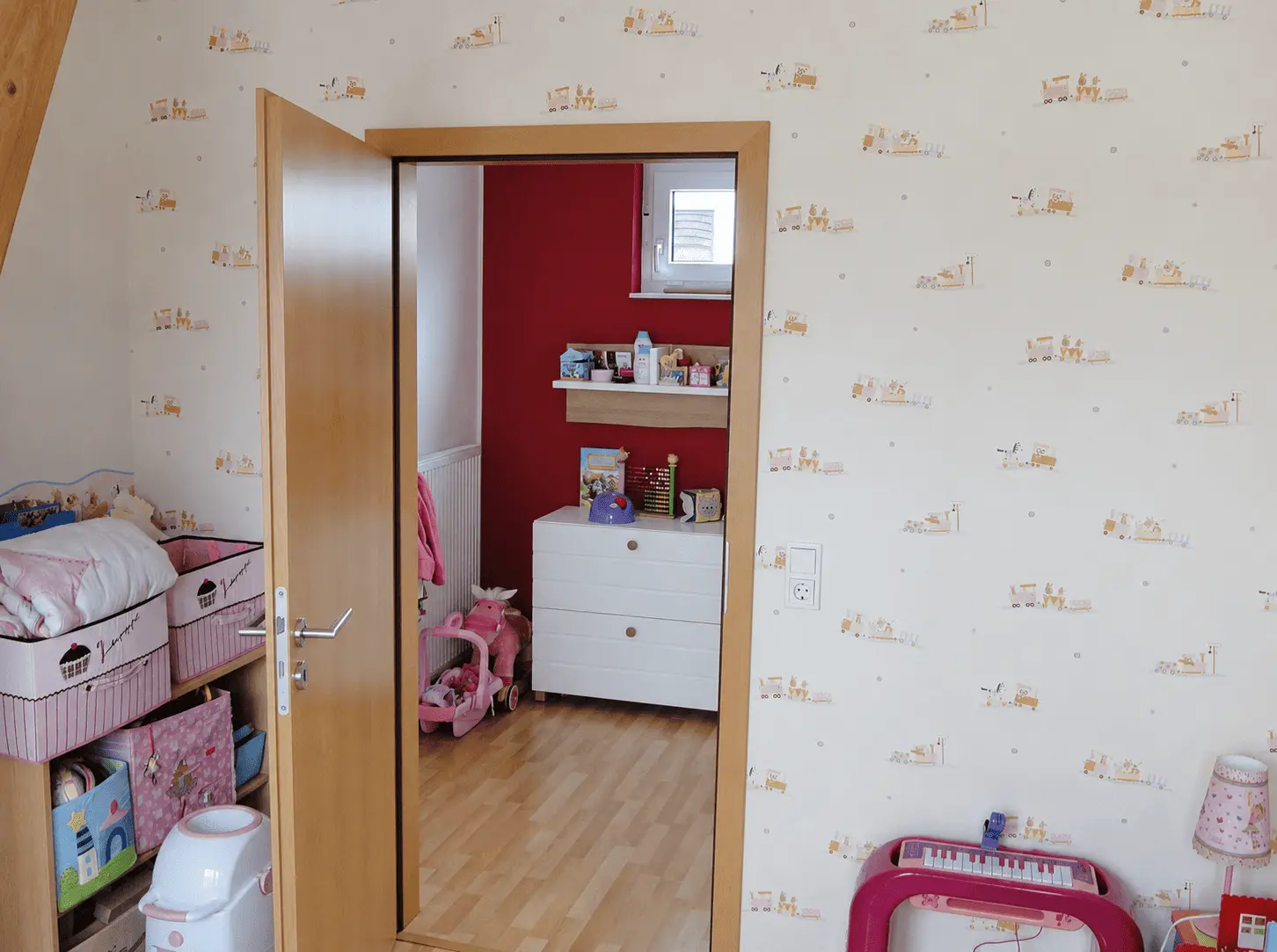 Kinderzimmer mit heller Zugtapete, Holztür und Blick in den angrenzenden Spielbereich