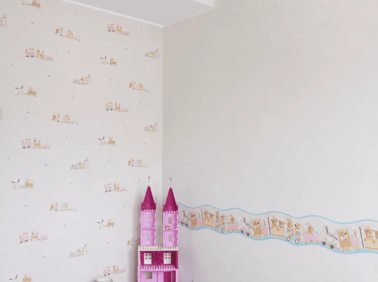 Helle Kinderzimmertapete mit Zugmotiven und Tierbordüre neben einem rosa Spielzeugschloss